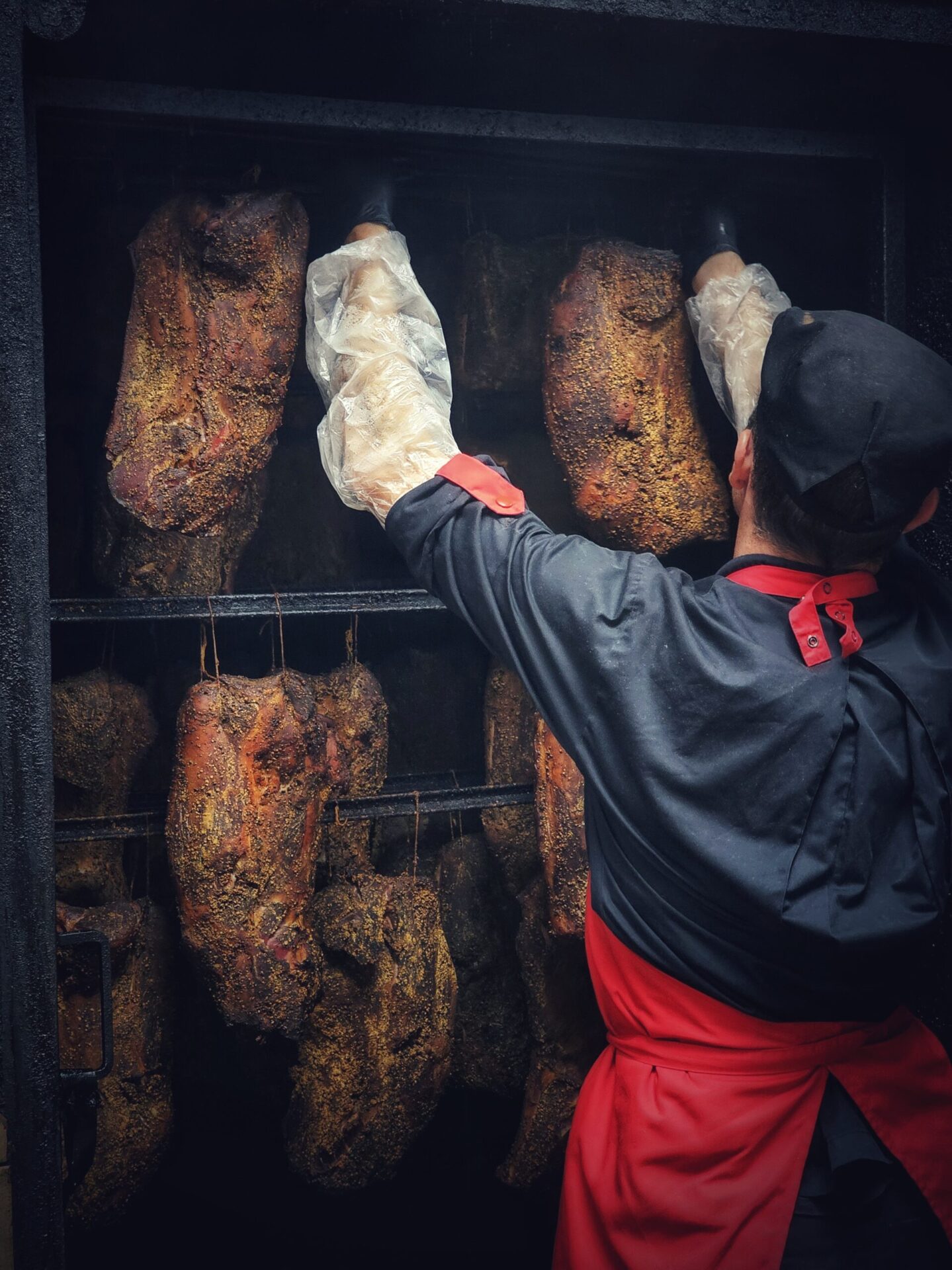 un charcutier qui accroche manuellement du jambon cru pour le fumage à l'ancienne