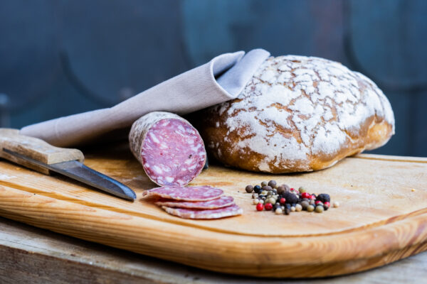 saucisson de cerf sur planche avec miche et couteau et graines de poivre
