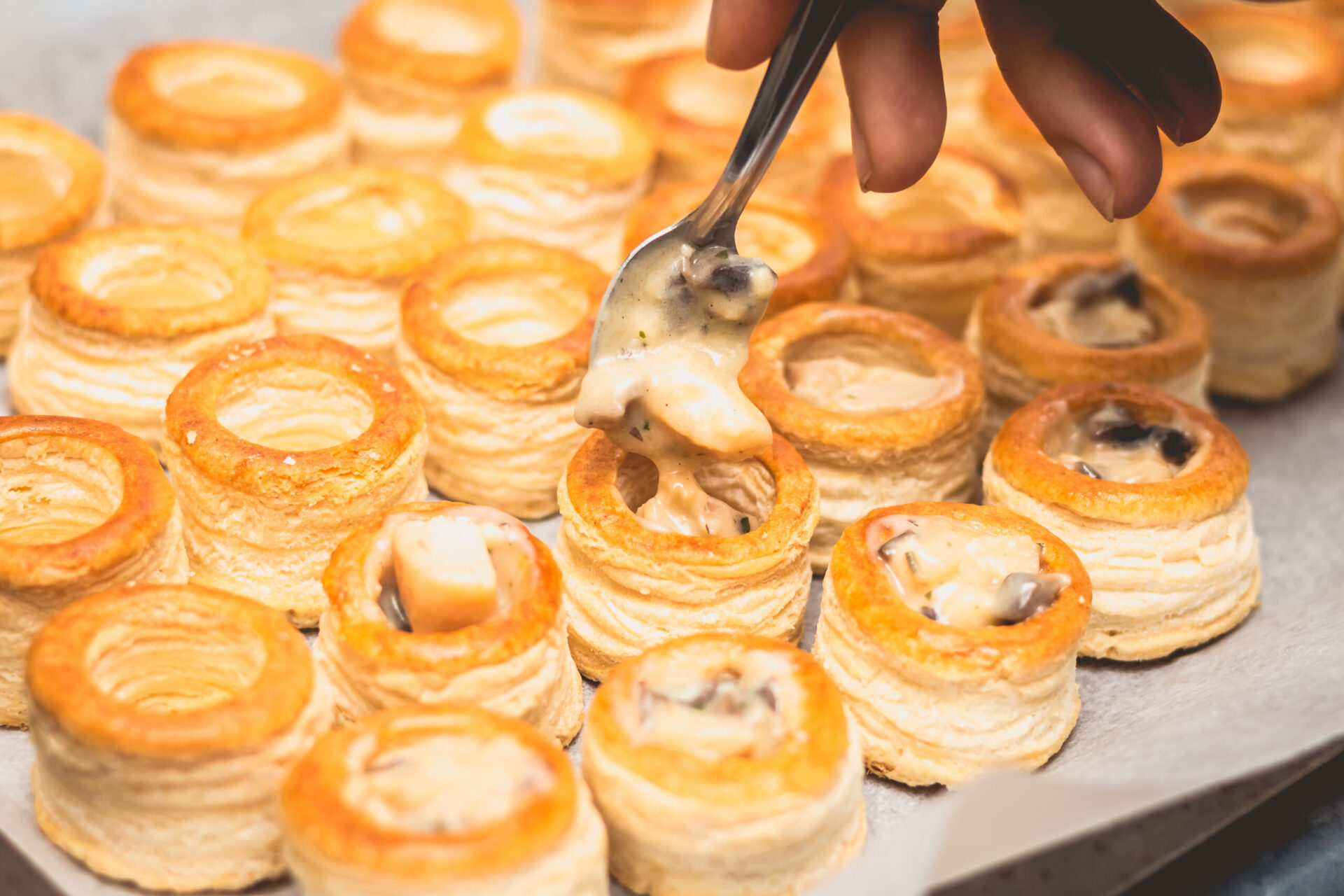 vol au vent disposés sur une table en train d'être rempli de bouchée à la reine
