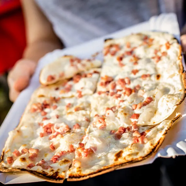 photo d'une tarte flambée rectangulaire portée par des mains
