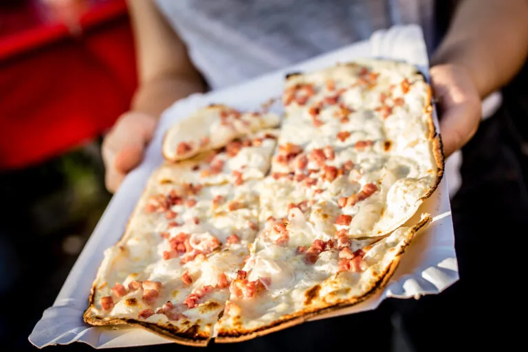 photo d'une tarte flambée rectangulaire portée par des mains